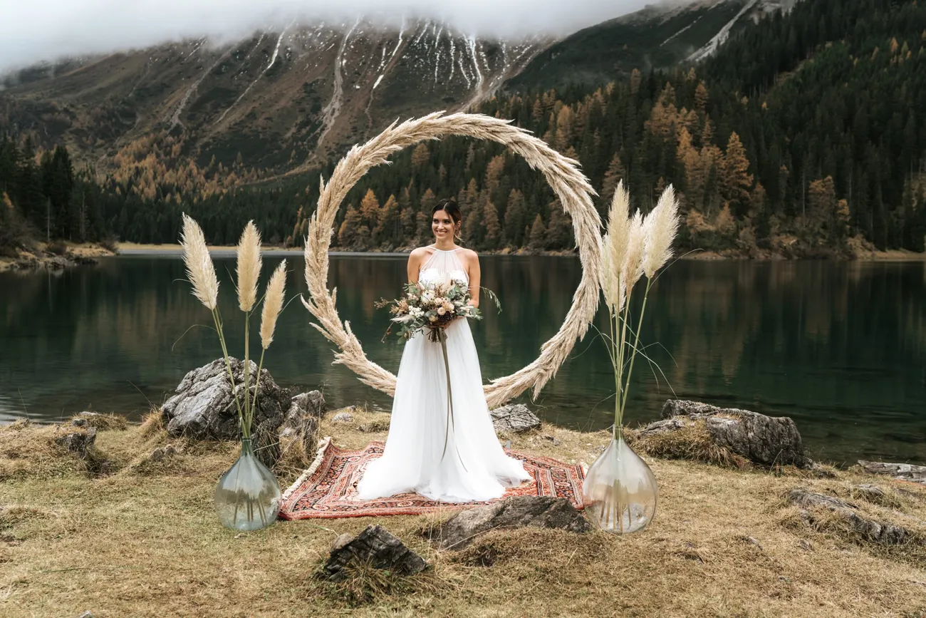 A pampas-grass arch set by a Tyrolean mountain lake with autumn larches