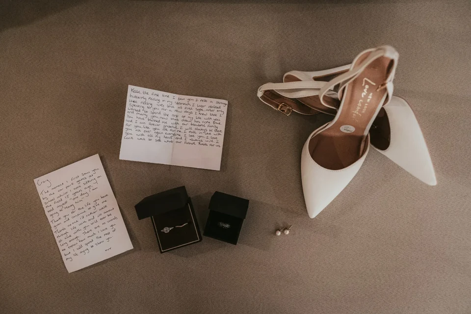 A flatlay of shoes, vow book and ring box