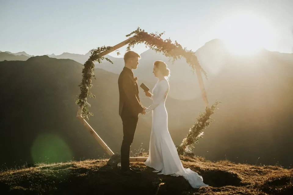 A sunset ceremony under a circular floral arch, the sun flaring through