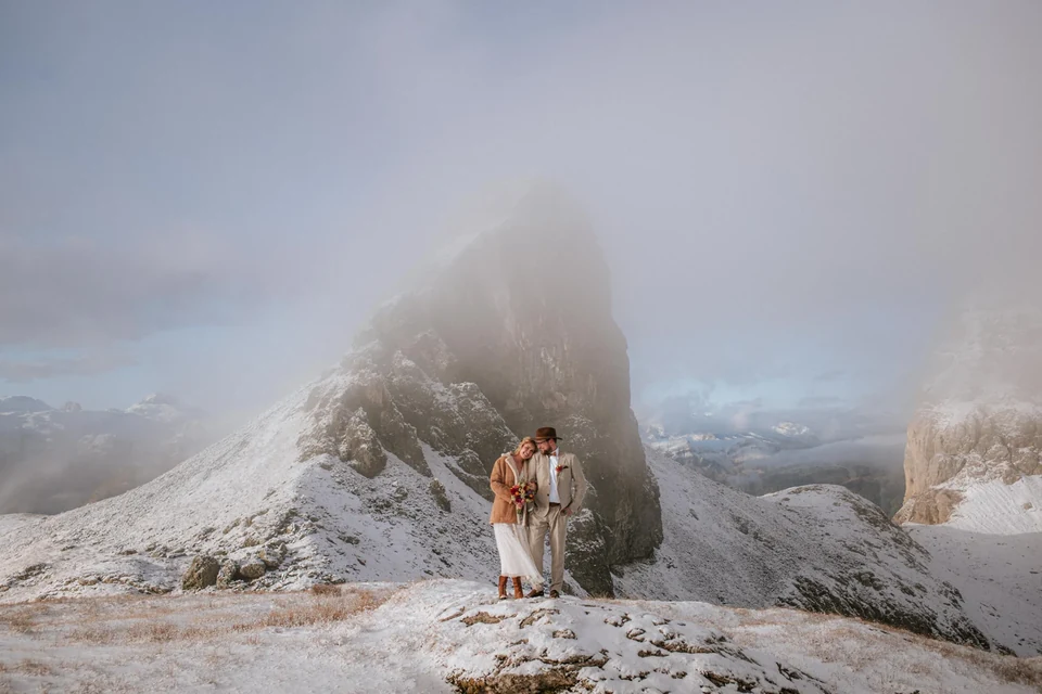 A couple kissing on a misty Dolomite ridge as a peak breaks the cloud
