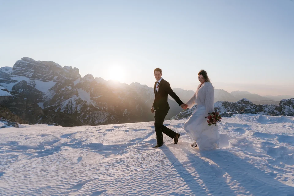 The couple walking through snow with the low sun behind