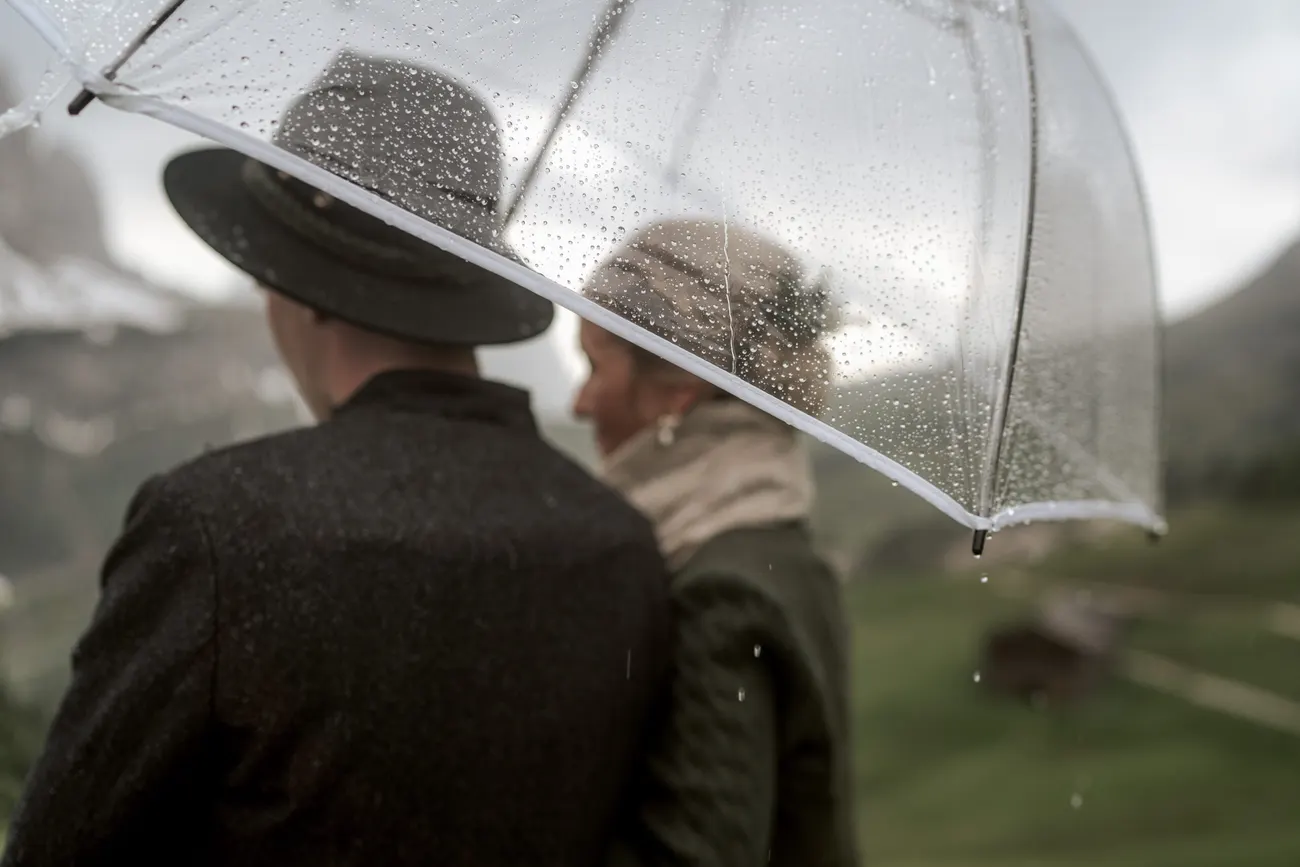 A bride in a dirndl smiling through mountain rain
